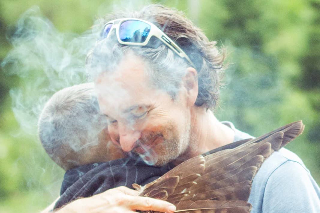 Zwei Männer umarmen sich im Rauch, ein Federflügel liegt auf dem Rücken