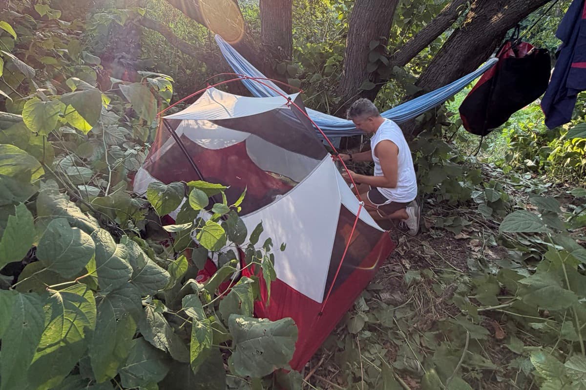 Ein Mann baut sein Zelt neben einer Hängematte im Auwald auf